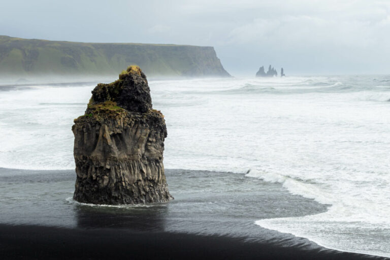 Lone sea stack on black sand, waves crashing